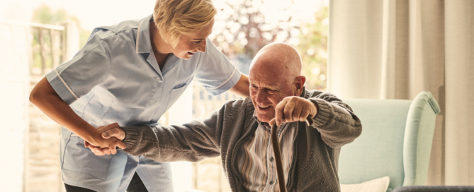 In-home caregiver assists elderly man with cane out of his chair while providing home care services