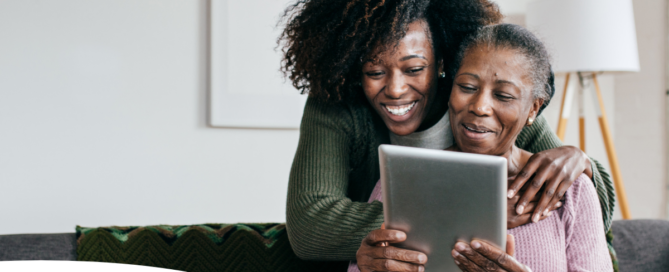 A caregiver helps a senior with her tablet, representing the rise of technology in home care.