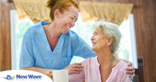 A caregiver and client smile while the caregiver hugs and helps the client, representing professional caregiving.