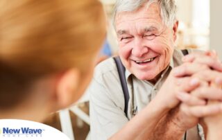 A caregiver holds hands with a happy older client, representing the results of creating a comfortable environment in the home.