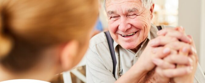 A caregiver holds hands with a happy older client, representing the results of creating a comfortable environment in the home.