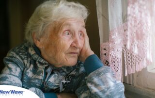 An older woman peacefully looks out of the window while the sun is still up, representing what can happen with sundowning.