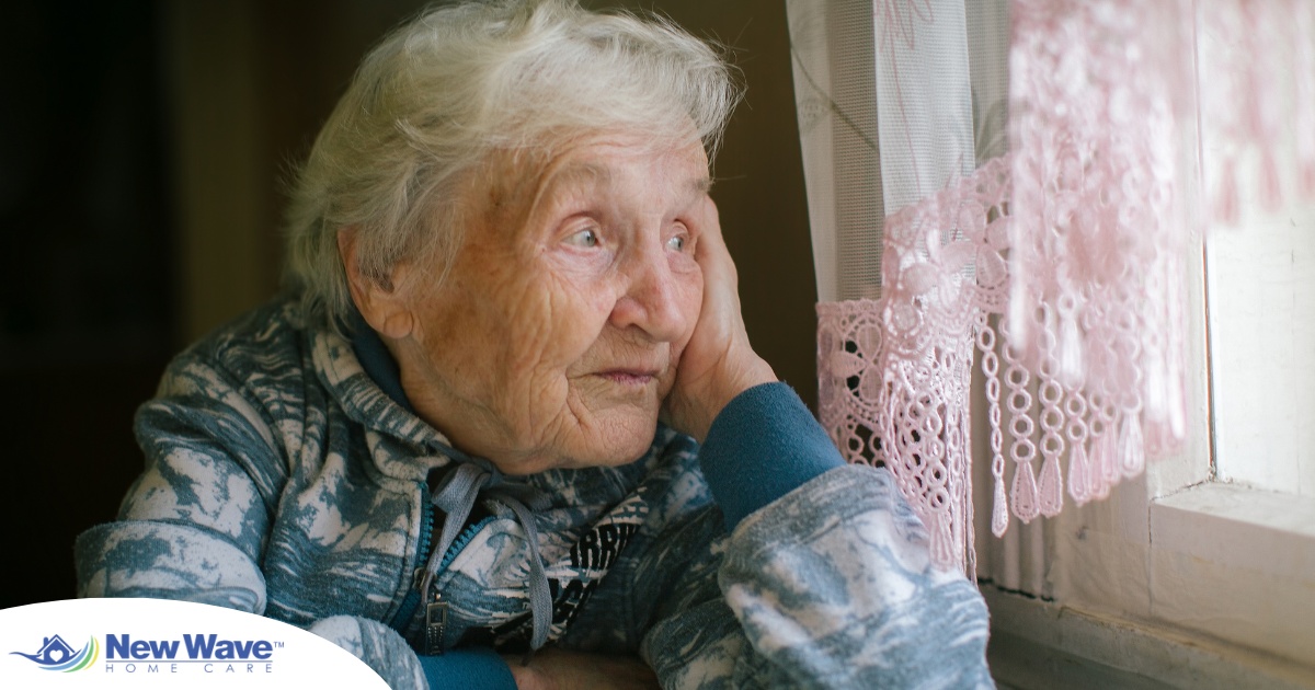 An older woman peacefully looks out of the window while the sun is still up, representing what can happen with sundowning.